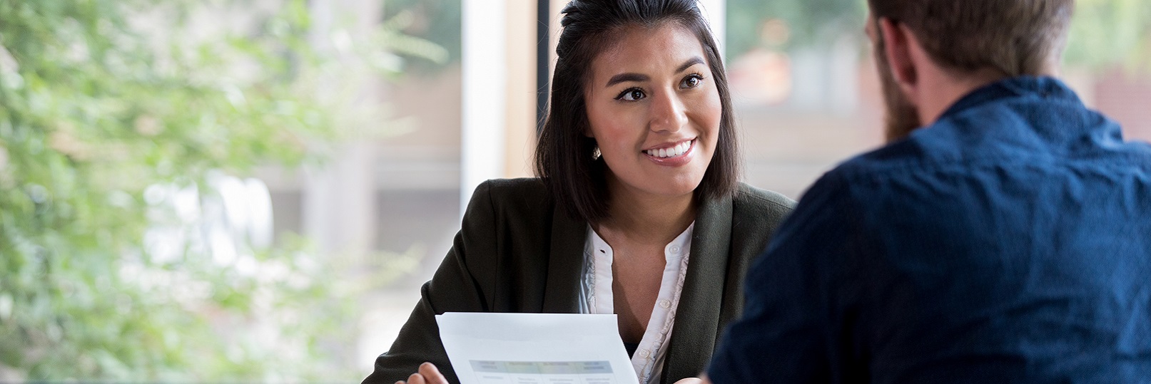 Woman holding paper sitting across desk from man.
